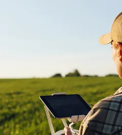 Close up of rear of Caucasian woman farmer in hat standing in green wheat field and controlling of drone which flying above margin.